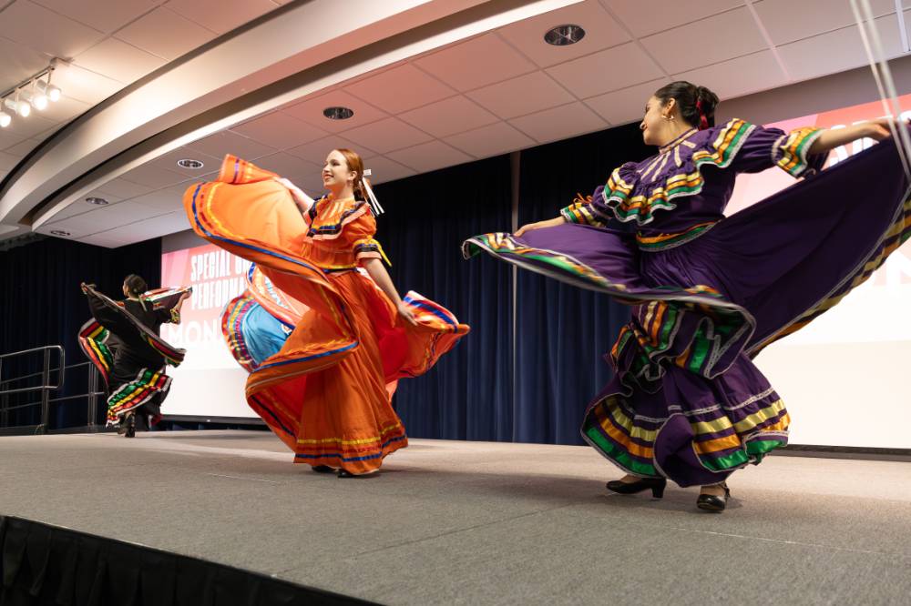 GVSU Monarcas traditional Mexican Ballet Folklorico performing on stage in purple and orange outfits.